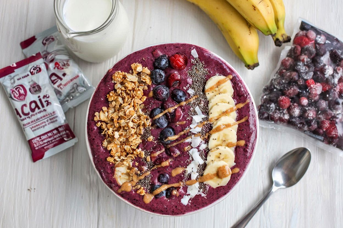 Vibrant acai smoothie bowl topped with fresh berries, banana slices, granola, hemp seeds, chia seeds, coconut flakes, and a drizzle of almond butter